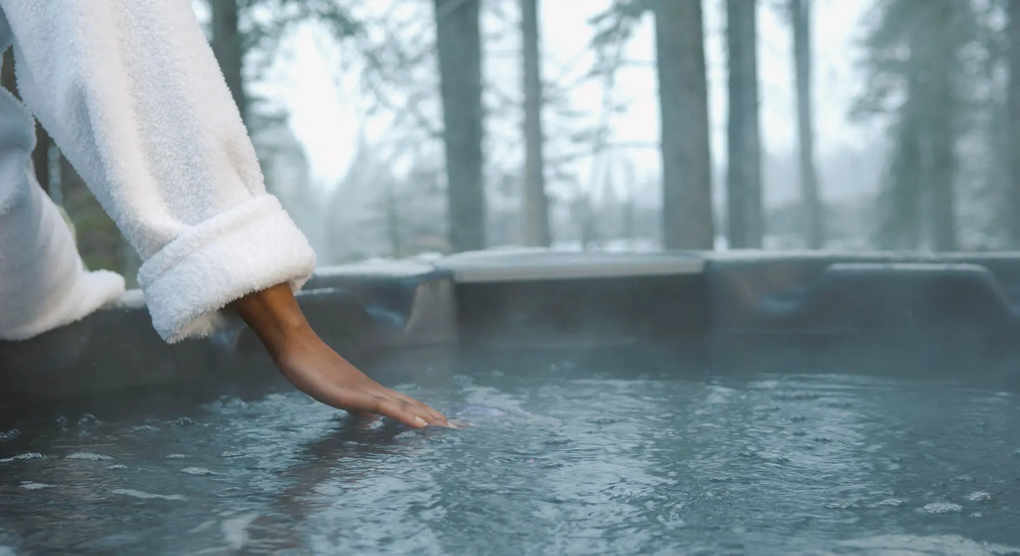 En kvinna i vit morgonrock som känner på det rykande vattnet i sitt spabad